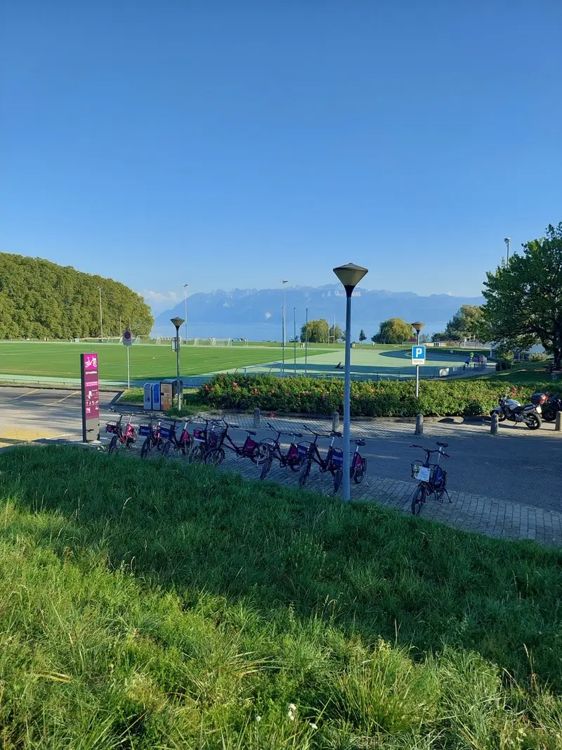 Bike-share station beside the EPFL sports fields, with Lake Geneva and the Alps behind