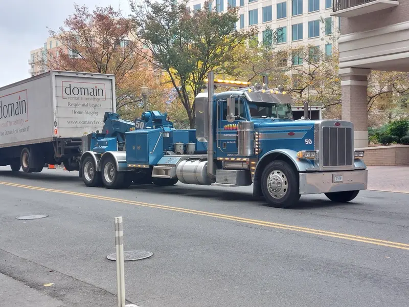 A big blue semi truck on a city street, with a white box truck behind it