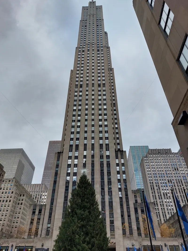 Looking up at the Rockefeller Center tower behind a large Christmas tree