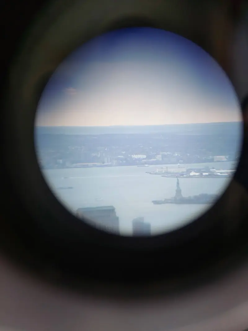 The Statue of Liberty, small in the harbor, seen through a binocular viewer