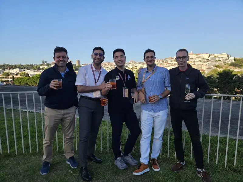Five people with drinks at a railing, the city on the hill behind them