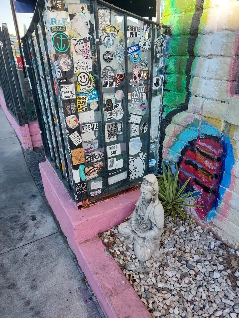 Sticker-covered railing, a colorful mural and a small stone statue outside the restaurant